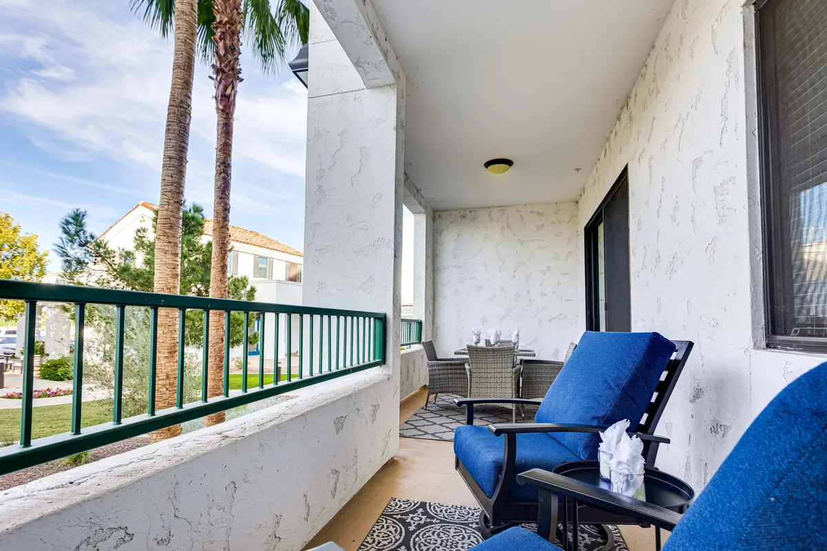 This patio scene features blue chairs arranged on a decorative rug, an outdoor dining set, and palm trees nearby. The mood is tranquil, suited for sipping coffee, reading, or enjoying friendly chats while taking in the view.