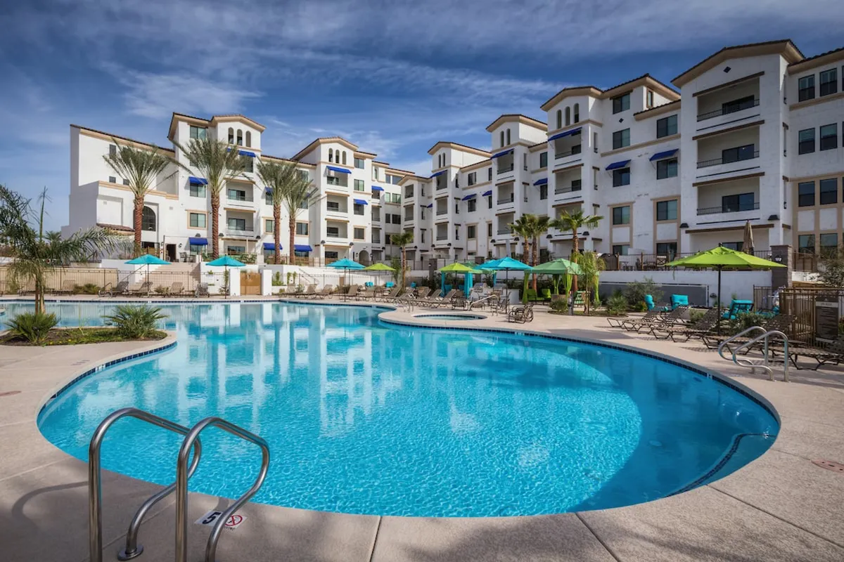 This vibrant exterior image captures the inviting swimming pool area surrounded by lounge chairs, umbrellas, the building facade, and lush landscaping. The atmosphere is relaxed and cheerful, suggesting both recreation and downtime after a productive day.