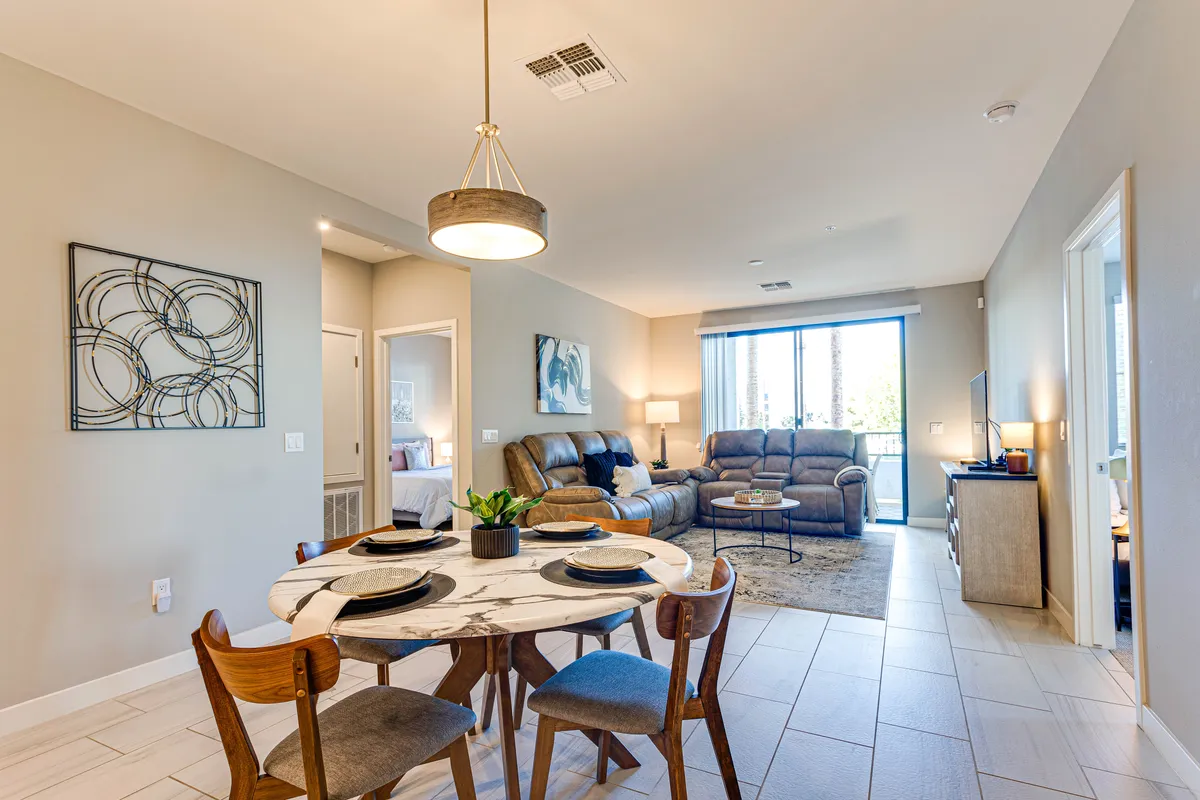 An open view of the dining table adjacent to a sofa area with a large window letting in natural light. The space bridges the dining and living areas, making it perfect for both meals and socializing. The scene evokes a cozy, welcoming atmosphere ideal for group activities.
