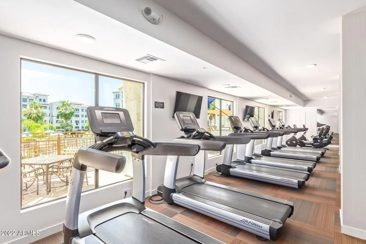 A motivating gym interior lined with treadmills facing large windows that let in natural light, and wall-mounted television screens for entertainment. The space is modern, well-equipped, and ideal for personal fitness goals.
