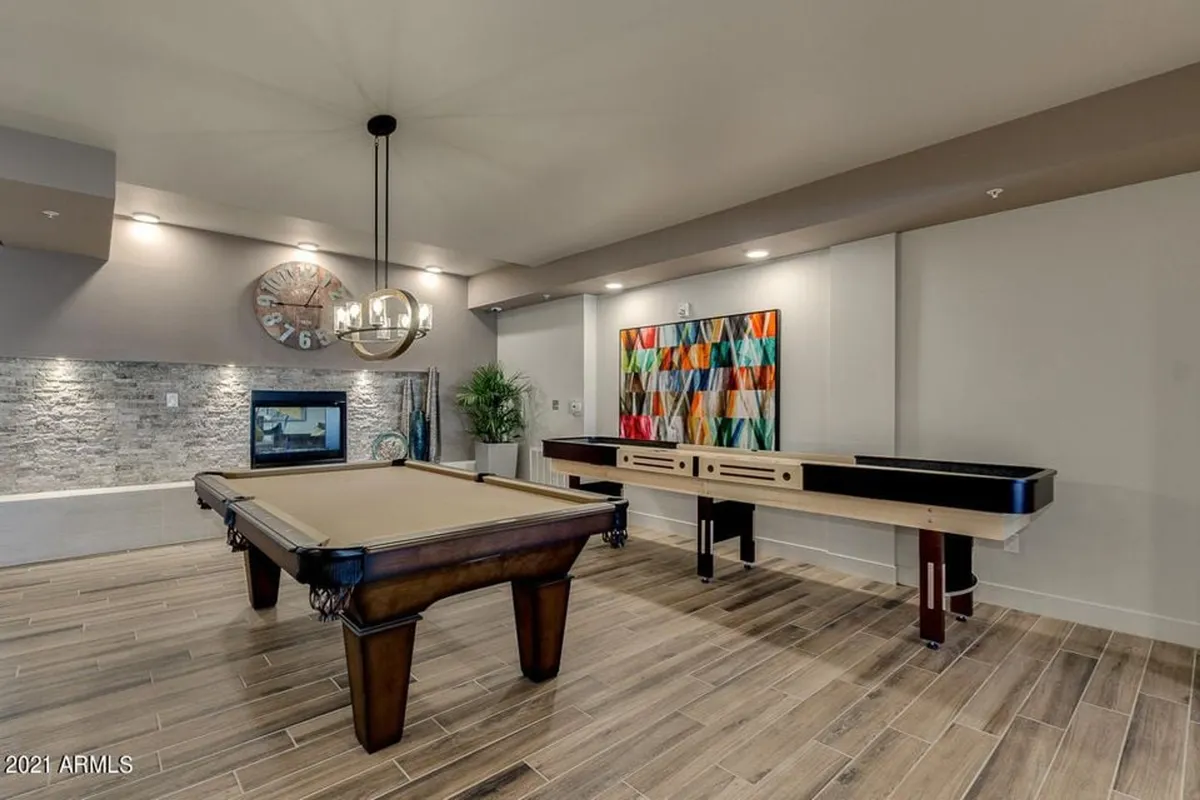 A vibrant interior clubhouse scene featuring a pool table and shuffleboard table set against a stone feature wall, with colorful wall art and modern lighting. The room exudes a playful energy, inviting residents to enjoy indoor recreation and social interaction.