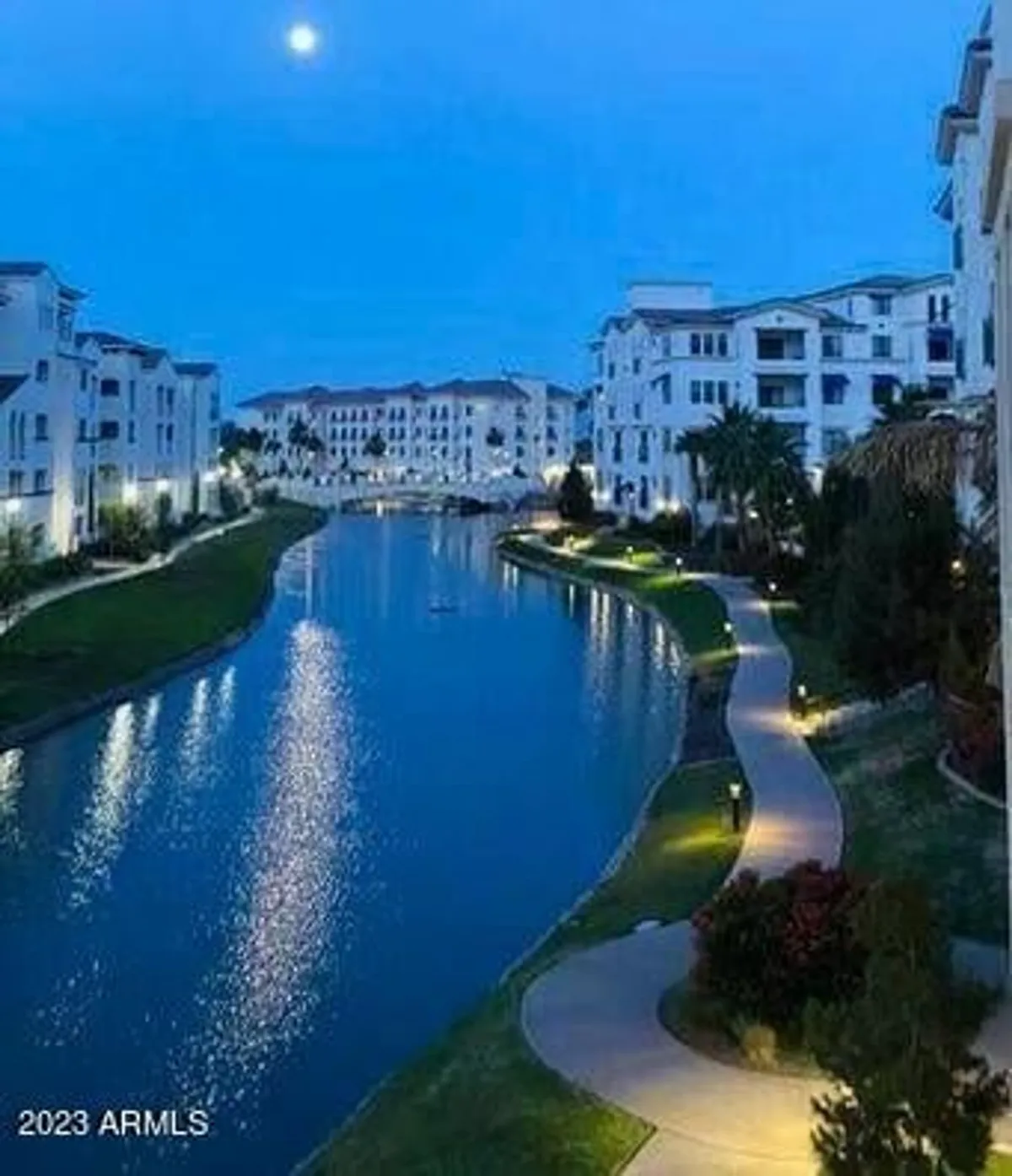 This exterior image captures a nighttime canal-side pathway illuminated by moonlight, with surrounding buildings visible in the background. The tranquil water reflects the evening sky, setting a serene urban scene ideal for evening strolls.