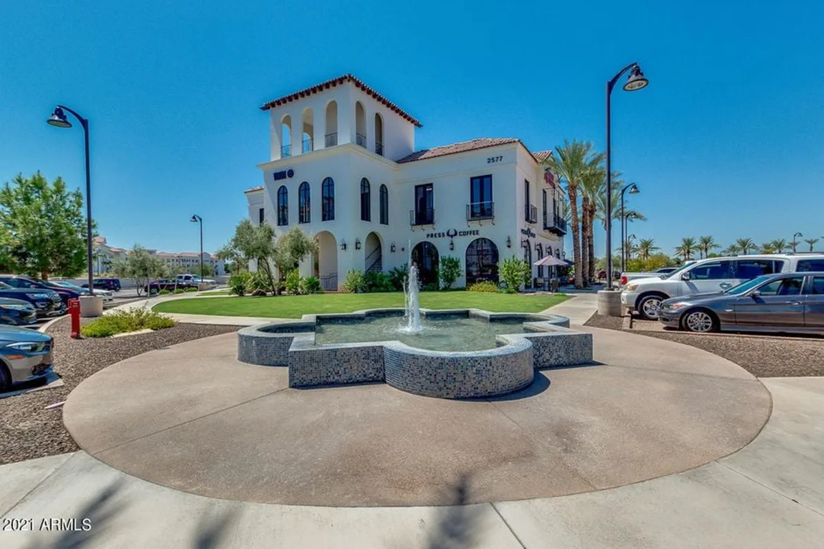 A stylish exterior plaza featuring a fountain, building facade, and lush landscaping. The space suggests a hub for outdoor gatherings, relaxation, and casual strolls, with people enjoying the pleasant environment.