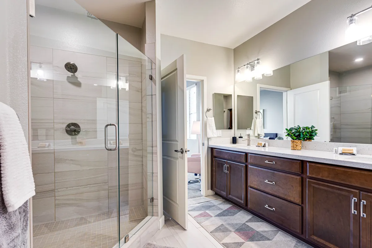 A spa-like ensuite bathroom featuring a glass shower enclosure, a double sink vanity with decorative mirrors, and subtle, soothing décor. The space exudes cleanliness and tranquility, evoking the feel of a luxury retreat.
