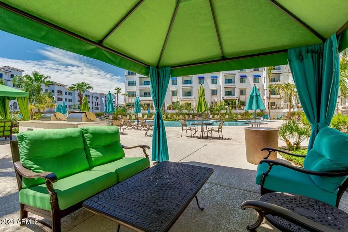 A bright and cheerful pool area featuring green seating, umbrella-shaded lounge chairs, and a sparkling pool. The scene invites both relaxation and social interaction, with plenty of comfortable spaces for reading, sunbathing, or informal gatherings.