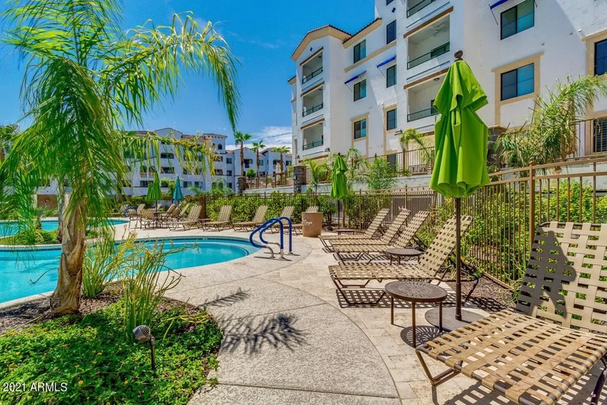 A bright, welcoming pool area with multiple lounge chairs, green umbrellas, palm trees, and tranquil water, creating an inviting space for socializing, relaxing, or unwinding outdoors.
